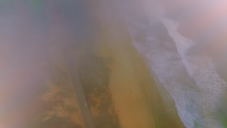 foamy waves coming to the sandy shore. drone descending through the fog over the road going by the beach.