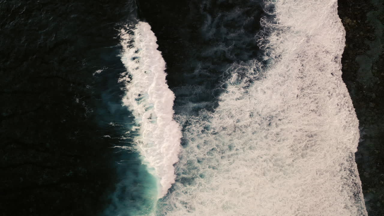 Aerial birds eye view of dramatic dark moody ocean water with white waves breaking