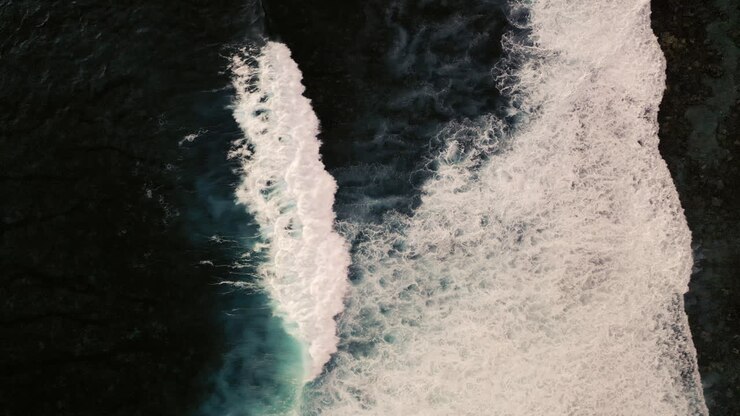 Aerial birds eye view of dramatic dark moody ocean water with white waves breaking