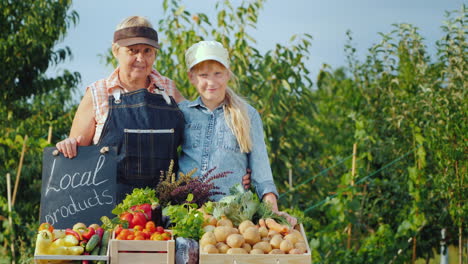 Portrait-Of-A-Grandmother-With-Her-Granddaughter-Behind-The-Counter-Of-A-Farmers-Market-Selling-Fres