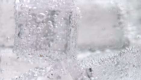 macro de cubitos de hielo de cerca en vidrio recubierto con burbujas y carbonatación a cámara lenta burbujeando agua con gas de soda