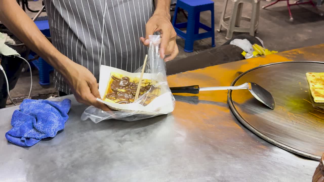 태국 푸켓의 거리 판매자는 밝은 조명 아래 초콜릿 으로 태국 로티를 준비하고 포장합니다.