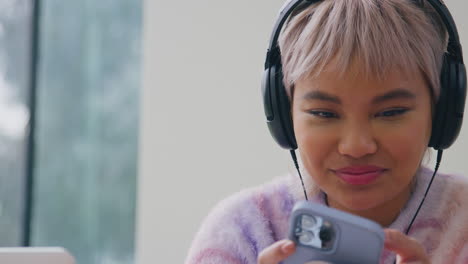 female vlogger wearing headphones with microphone live streaming looking at mobile phone