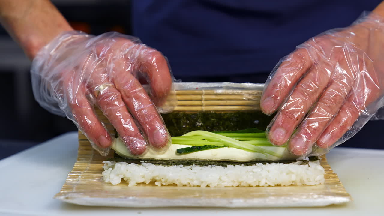 Sushi cooking process at restaurant. Close up of chef hands in gloves cooking sushi rolls in the kitchen