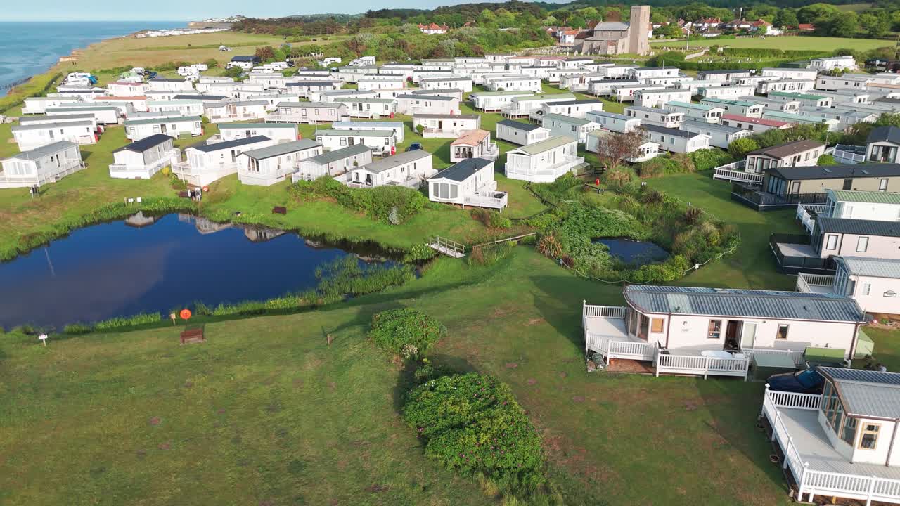 Rows of white holiday cottages with small ponds on green coastal land, Sheringham