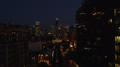 subway train approaches station platform at night, chicago skyline in background