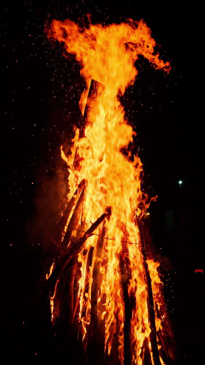 Wood burning in a bonfire at night with a distant view of the mood on the background. Vertical