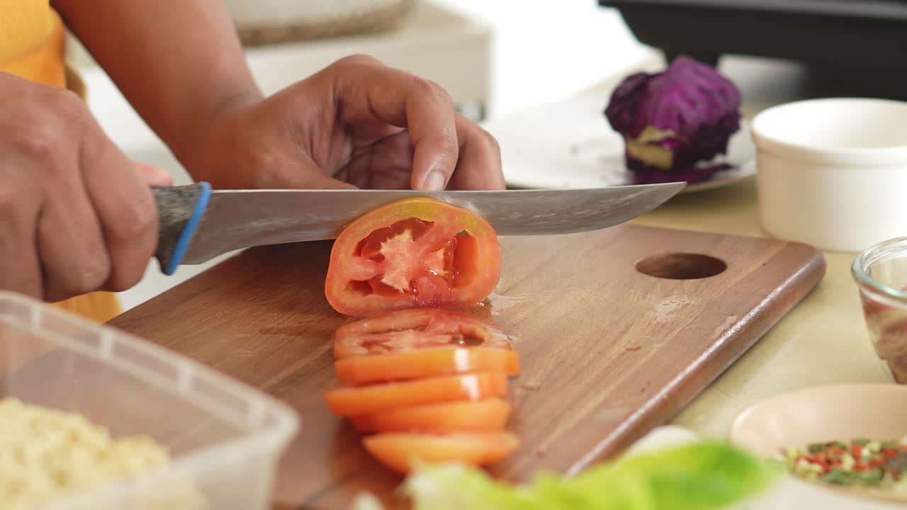 Person slicing a tomato on a cutting board in a kitchen