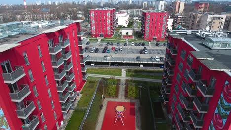 Nuevos-Edificios-Rojos-Con-Rosas-Pintadas-En-Un-Complejo-Residencial-Seguro-Con-Estacionamientos-Y-Un-Parque-Infantil-Durante-El-Verano-En-Polonia