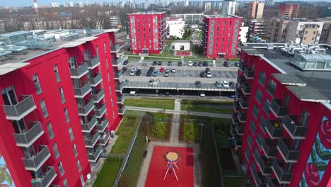 new red buildings with painted roses in a secure residential complex with parking lots and a playground during the summer in poland