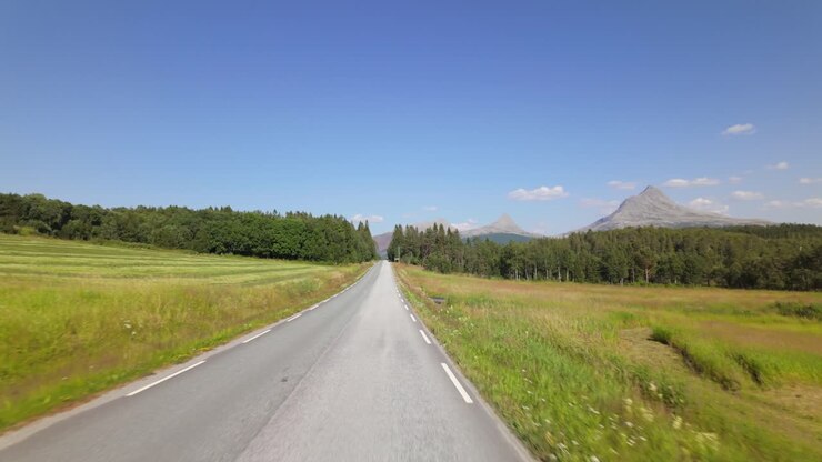 Guidare attraverso campi verdi verso montagne maestose in una giornata di sole