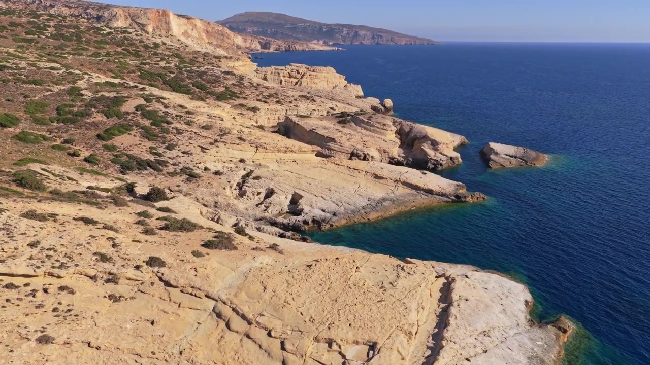 Vista aerea con drone di una costa rocciosa aspra e chiara con piccole insenature lungo il mare blu profondo, Matala, Grecia
