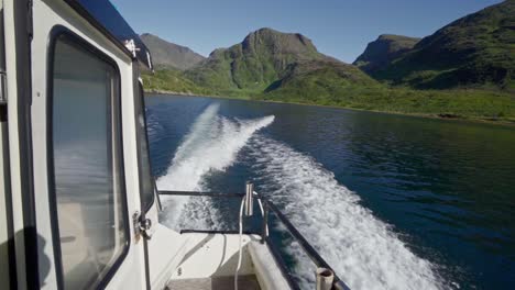 Back-view-of-a-boat-leaving-the-green-mountain-shoreline-of-Norway---Wide