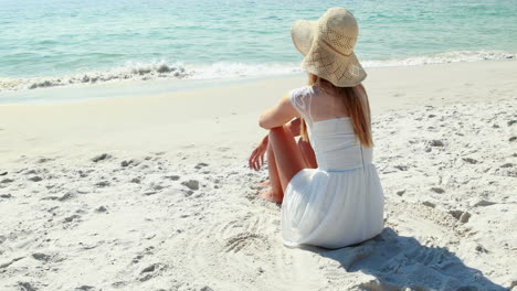 Vista-Trasera-De-Una-Mujer-Rubia-Sentada-En-La-Playa-Y-Mirando-El-Océano