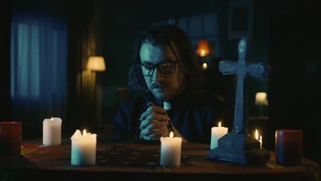 video capturing a table with magical tools on it a priest is sitting at the table with beads in his - video capturing a table with magical tools on it. a priest is sitting at the table with beads in his hands, praying with his eyes closed, when a hand lays on his shoulder. creative content, hallowee