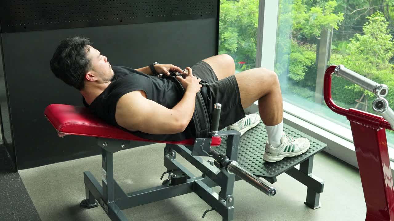 A man exercises with a barbell hip thrust on a bench in a well-lit gym overlooking greenery