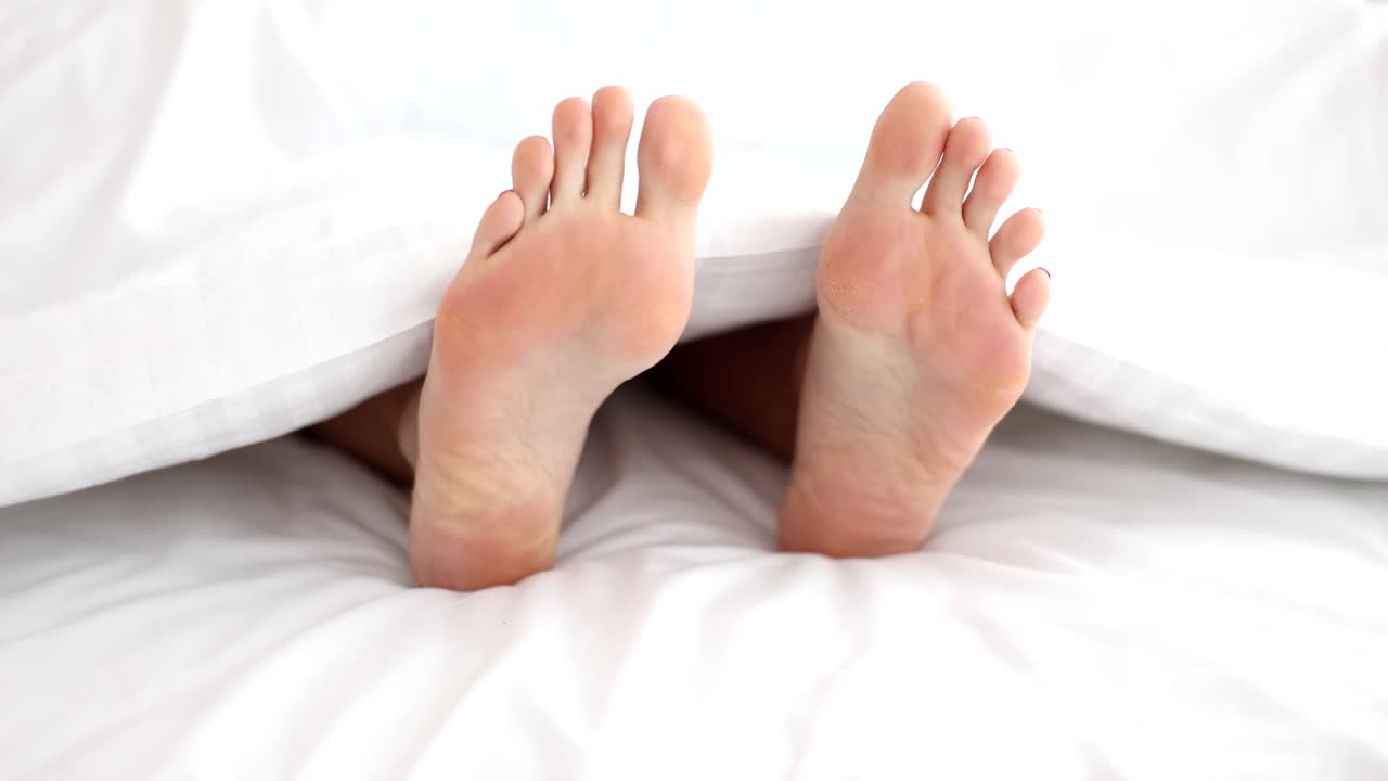 Feet under white sheets in bed