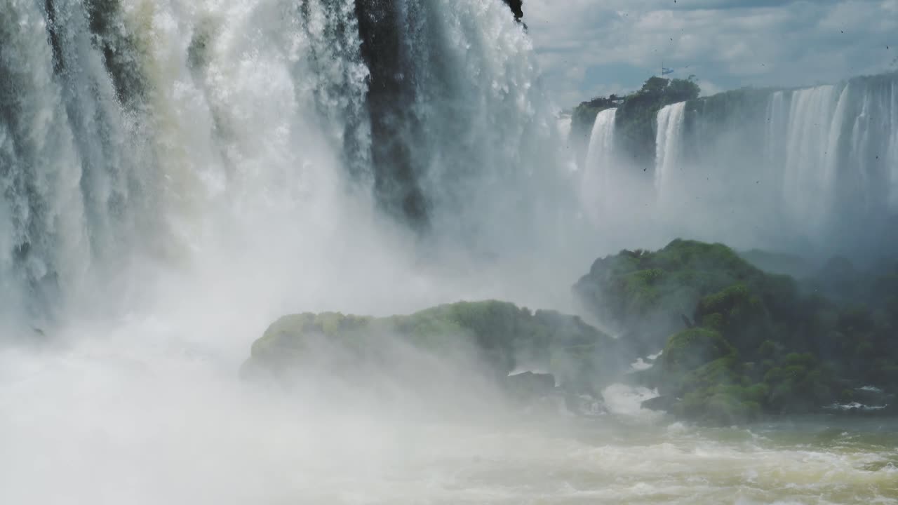 vista de cerca de la cámara lenta las cataratas de iguacu en el hermoso valle de la selva tropical, grandes rocas de musgo bañadas en aerosoles de salpicaduras de agua que cae desde el borde de altos acantilados en brasil, américa del sur