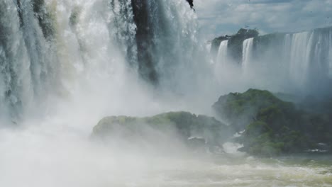 close up view of slow motion iguacu falls waterfalls in beautiful rainforest valley, mossy large rocks showered in spray from splashing falling water from tall cliff edge in brazil, south america