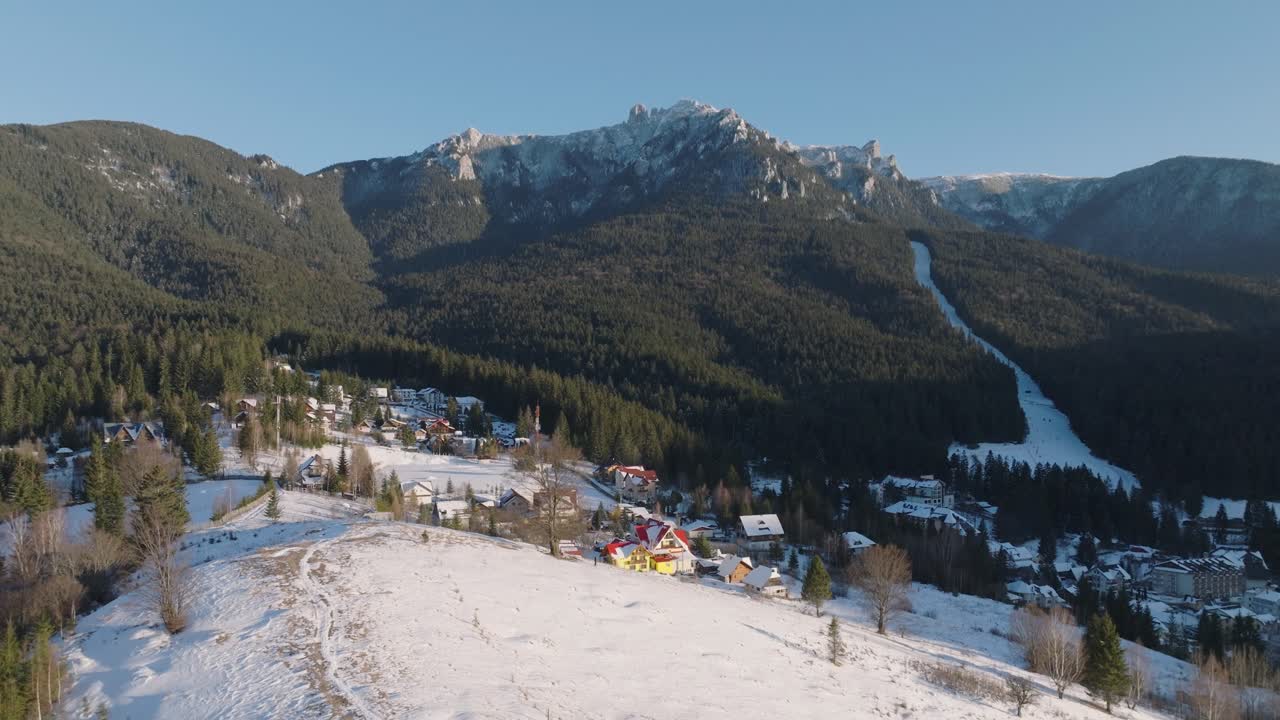 Snow-covered village at the base of a forested mountain on a sunny winter day