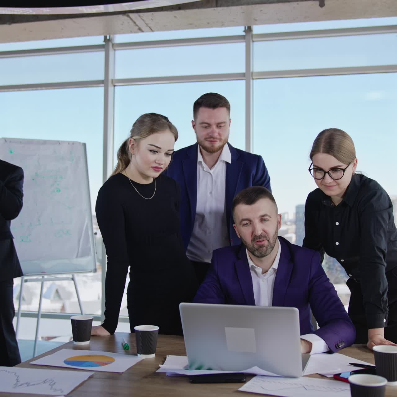 Teamwork and brainstorming at office meeting. Colleagues gathered around their chief and look at his laptop. Male manager speaks on the phone at backdrop