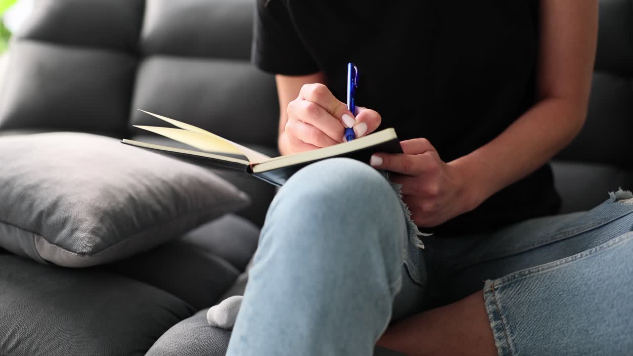 Una persona che scrive su un quaderno mentre è seduta su un divano