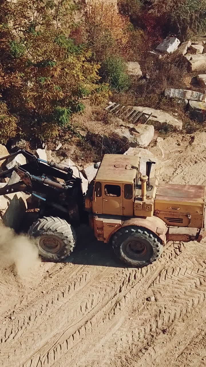 professional bulldozer with a bucket is spreading sand near the stones on the background of the quarry. Close-up. Vertical video