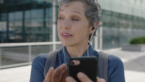 portrait of mature professional business woman waiting in city listening to music on earphones texting browsing using smarphone mobile technology in city