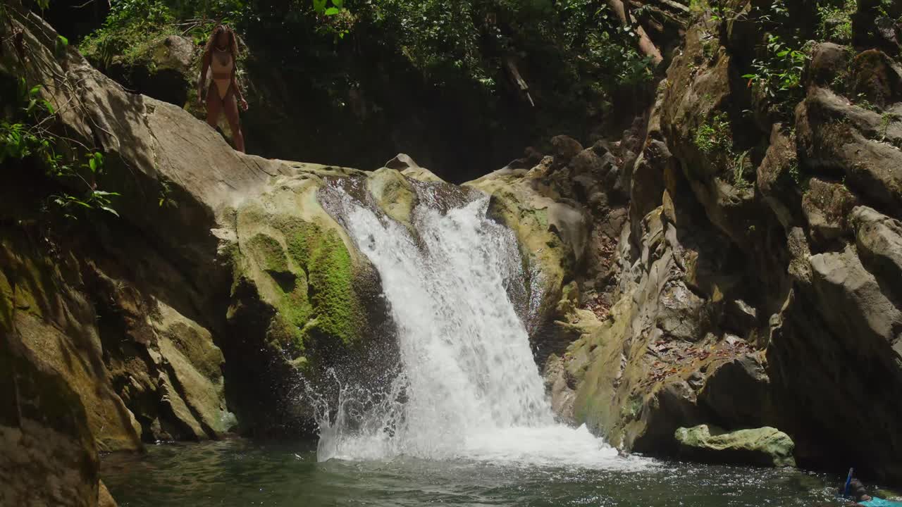 Two girls in bikinis find bliss at a tropical waterfall and river in the Caribbean.
