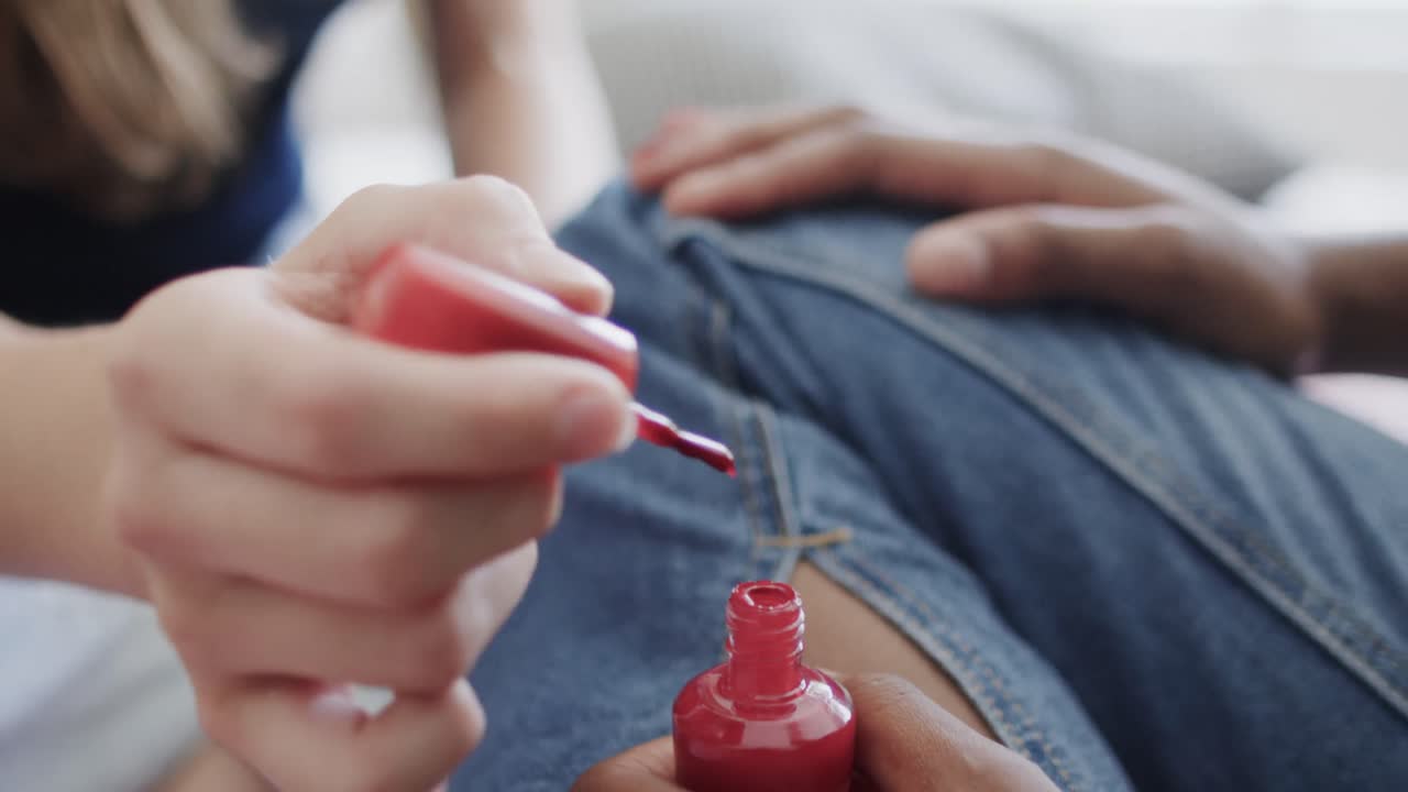Diverse teenage female friends sitting on bed painting each other's fingernails