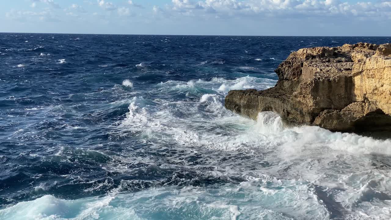 las olas tempestuosas se estrellan contra el acantilado de piedra caliza en cámara lenta, la luz de la tarde soleada
