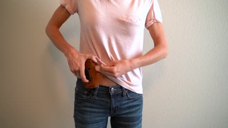 slow motion of a woman placing a holstered handgun in her waistband to conceal it