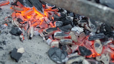 close-up of glowing and fuming hot coal that is resting on the floor of an outdoor grill