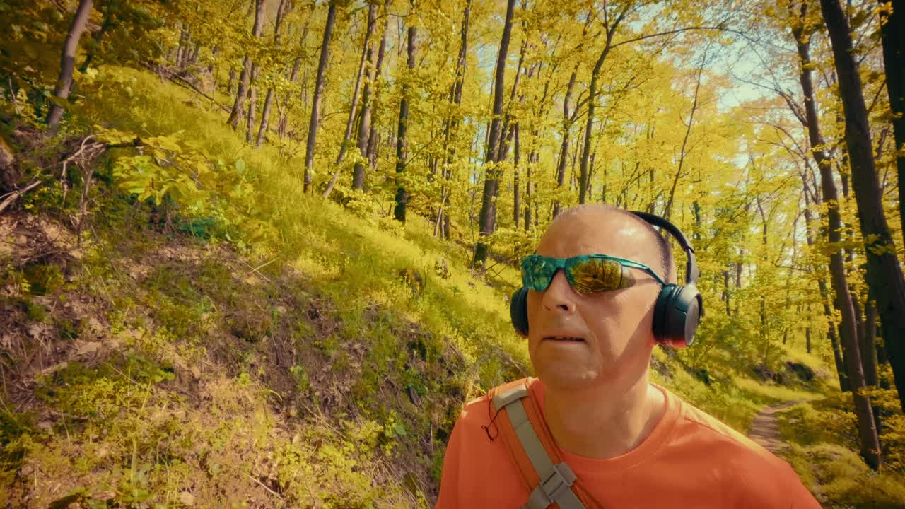 Un uomo maturo e rilassato sulla cinquantina ascolta musica in cuffia durante un'escursione. Concetto di sollievo per la salute mentale, riduzione dello stress e pace nella natura. Filmato 4K di alta qualità.