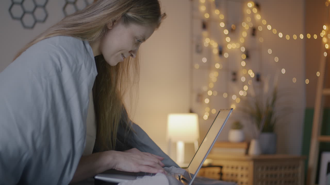 Woman working on laptop at night in a cozy bedroom