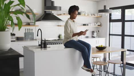 Feliz-Mujer-Afroamericana-Usando-Un-Teléfono-Inteligente-En-La-Cocina