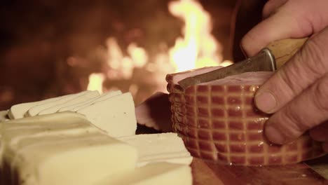 cured ham is cut into thick slices on board near flaming hot camp fire