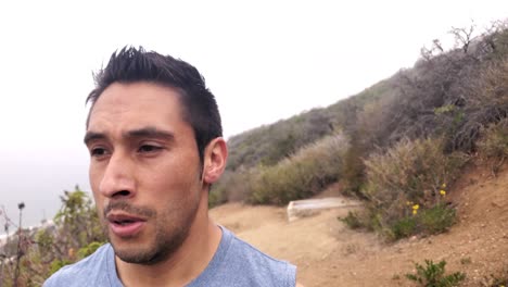 A-male-finishes-his-workout-and-looks-out-over-the-trail,-mountain-and-ocean-in-accomplishment