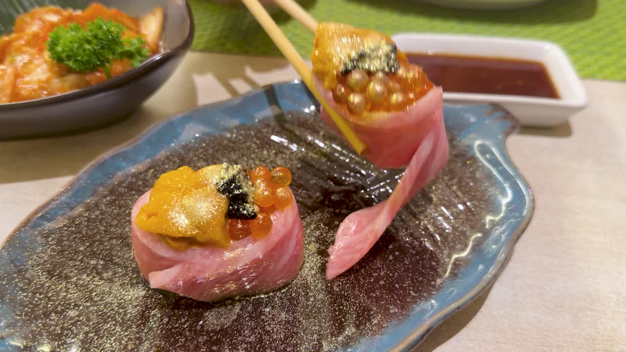 箸がウニとキャビアを乗せたプレミアム和牛ロールを皿から持ち上げている。