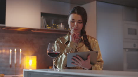 a woman using a tablet in a cozy kitchen with wine and candlelight