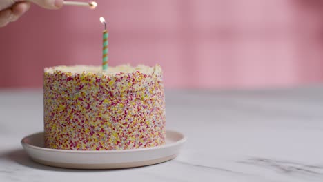 single candle being lit by hand on studio shot of birthday cake covered with decorations 1