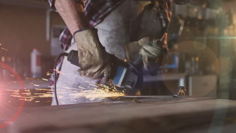 animation of glowing light over caucasian man using grinder in workshop