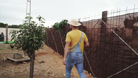 un joven granjero con sombrero caminando por su granja entre sus pollos y árboles