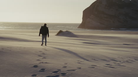 man walking on a sandy beach at sunset