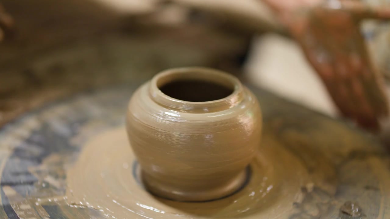 Close-up of hands molding wet clay into a ceramic vessel on a spinning wheel.
