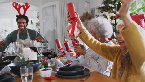 multi generation family pulling christmas crackers as they sit for meal at table