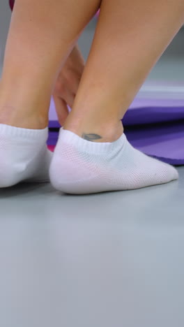 primer plano de las piernas inferiores en calcetines blancos de tobillo caminando hacia la alfombra de yoga en un estudio de fitness moderno, el espejo refleja el entorno mientras la persona arrastra la alfombra, el fondo presenta equipos de entrenamiento