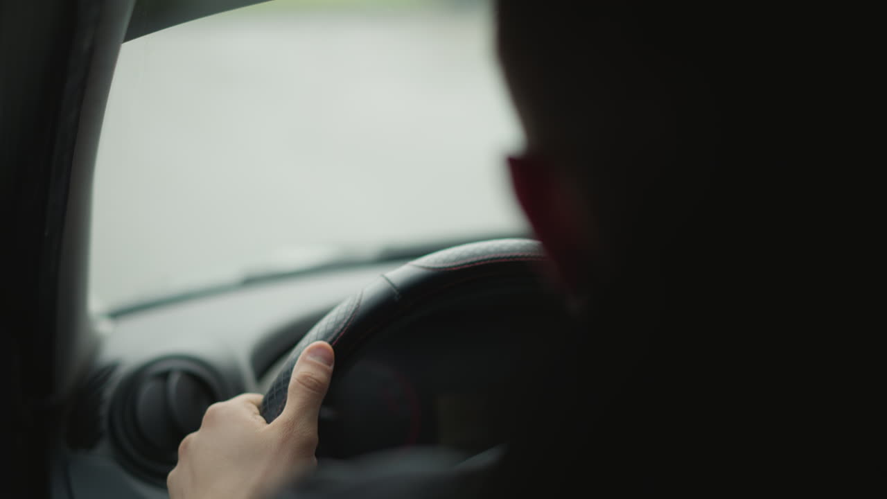 Back view of urban explorer driving with hands on steering wheel, interior shot framed to emphasize control and focus during chilly city commute, blurred street scene beyond windshield adds mood