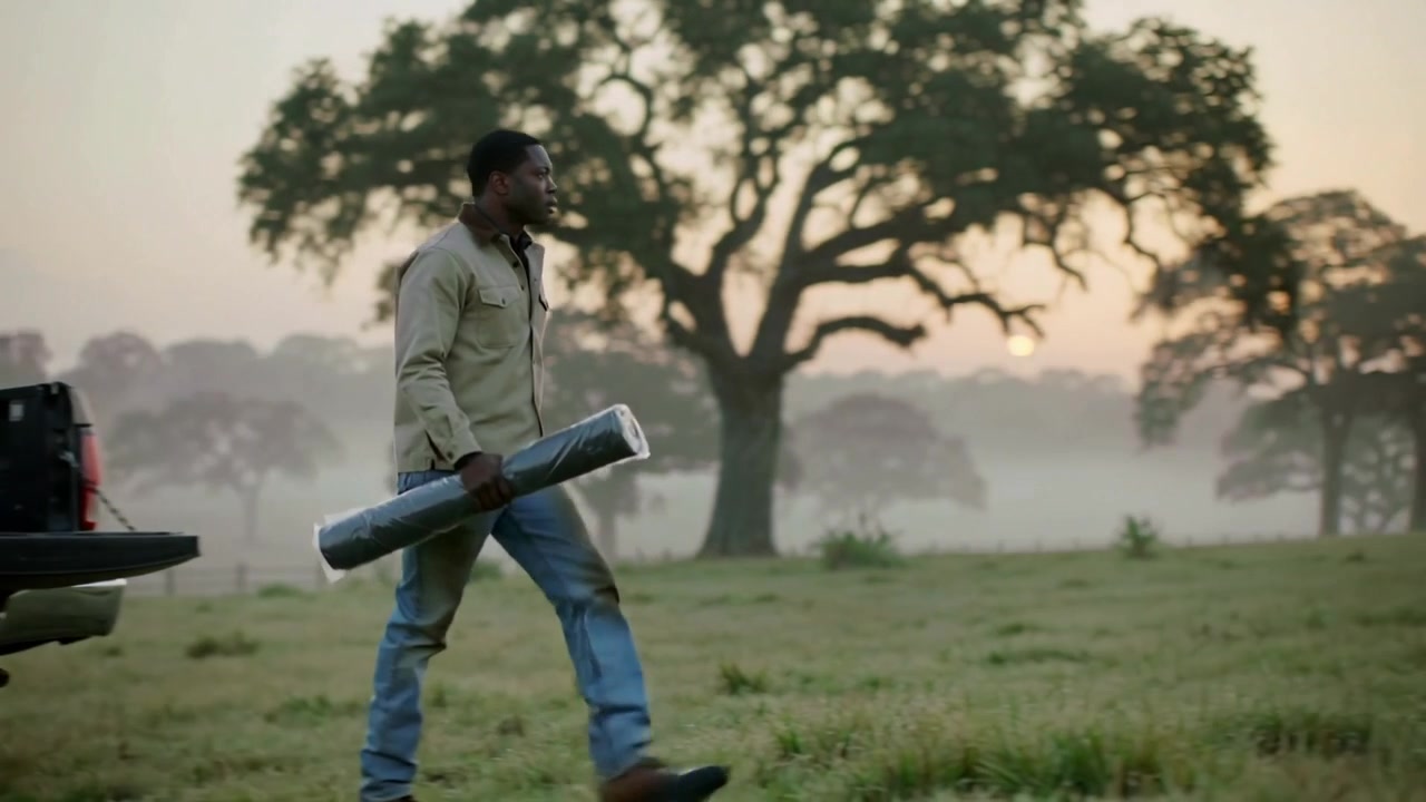 Leaving truck tailgate, dawn urging man in boots walking across misty pasture holding rolled tarp