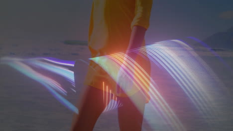 Wearing yellow dress, person creating animation with colorful light trails on beach